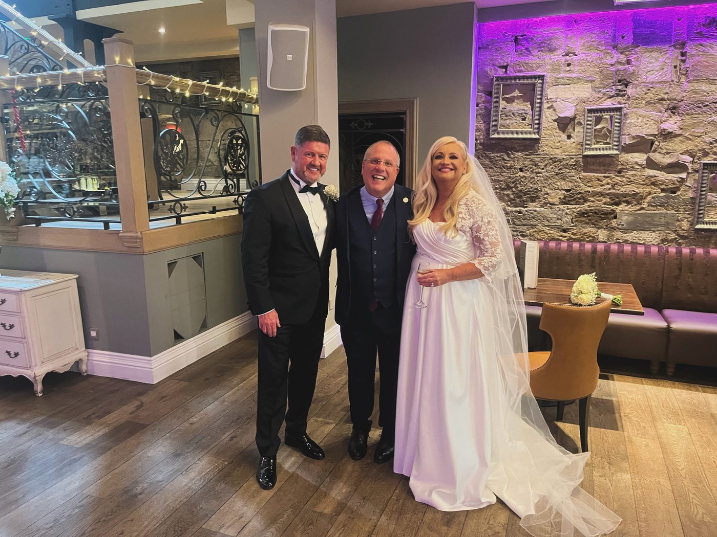 John Paul with a bride and groom at Citation, fairy lights and stone walls behind them