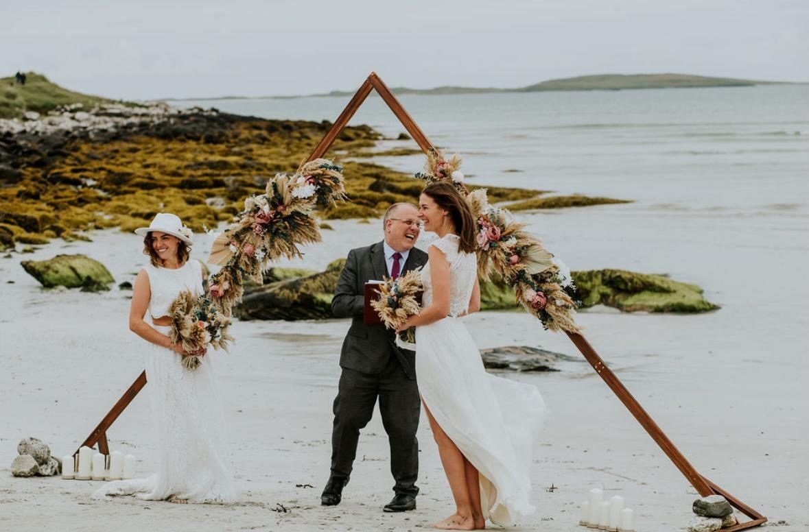 A beach wedding ceremony on South Uist — triangle arch dressed in dried flowers on white sand, the Atlantic behind
